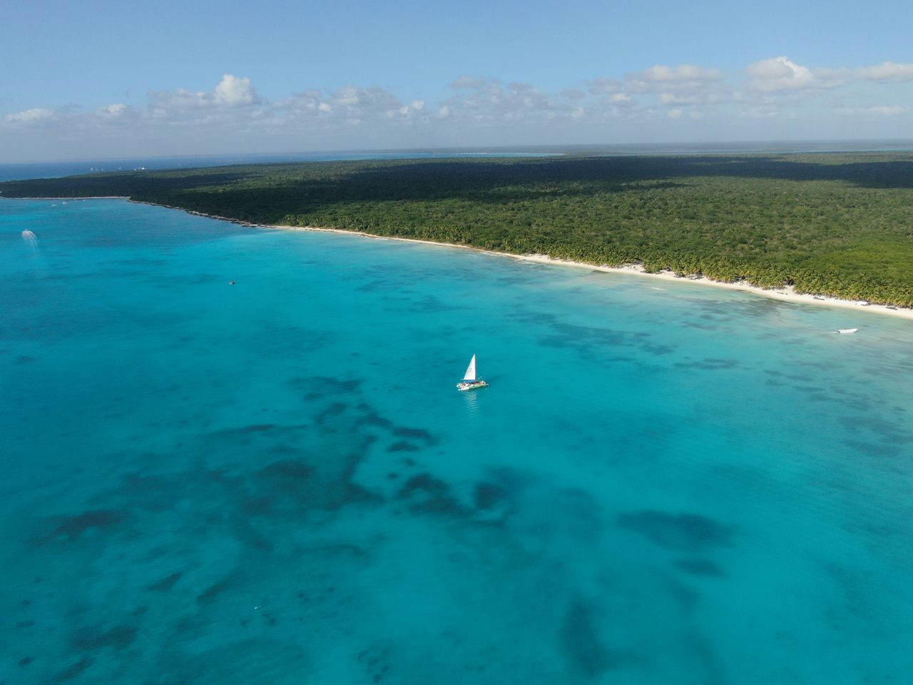 Stunning aerial view of a sailboat gliding on the clear turquoise waters of the Caribbean Sea near a lush coastline.